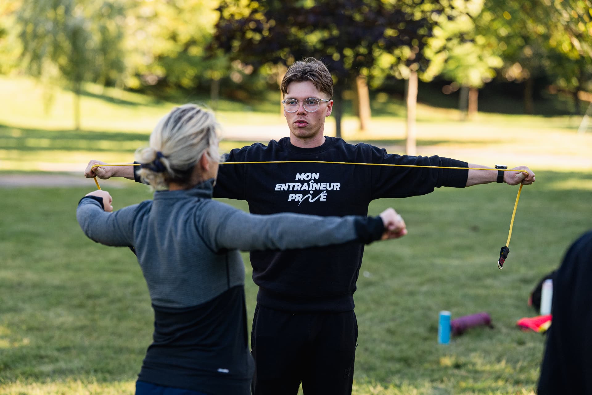 Kinésiologue guidant une participante dans un exercice avec un élastique en plein air